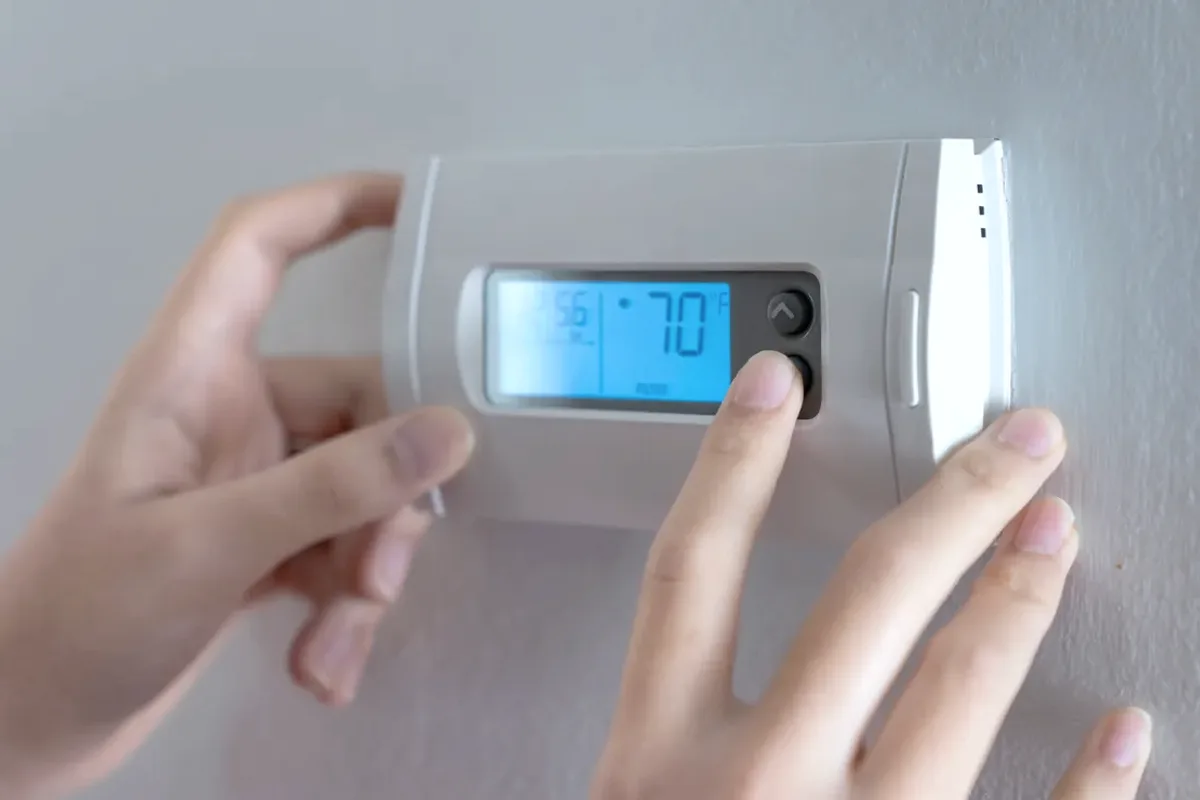 Hands adjusting a digital wall thermostat
